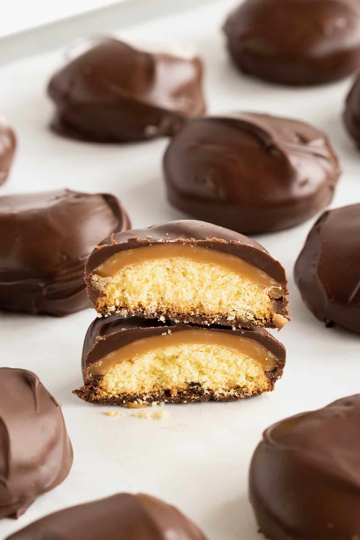 Homemade Twix bites on a parchment lined surface. One bite is cut in half with both halves stacked together to reveal the inside of the candy.