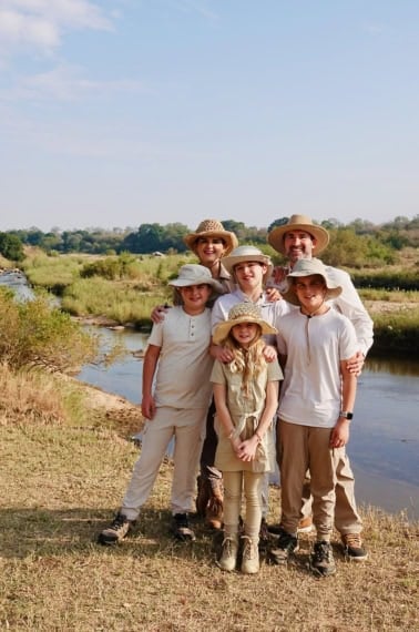 The Brown family wearing white shirts and khaki pants and wide brimmed hats standing by a river.