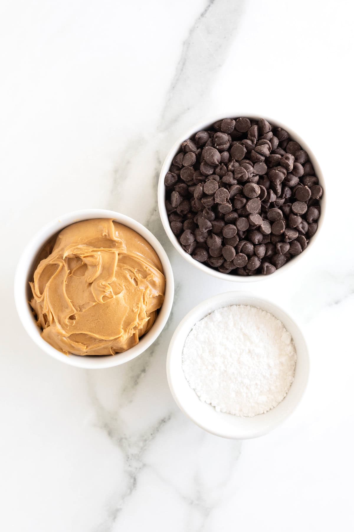 Ingredients to make peanut butter cups in small white dishes on a white marble counter.