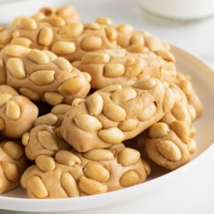 A large white plate of payday candy bar bites on a white counter.