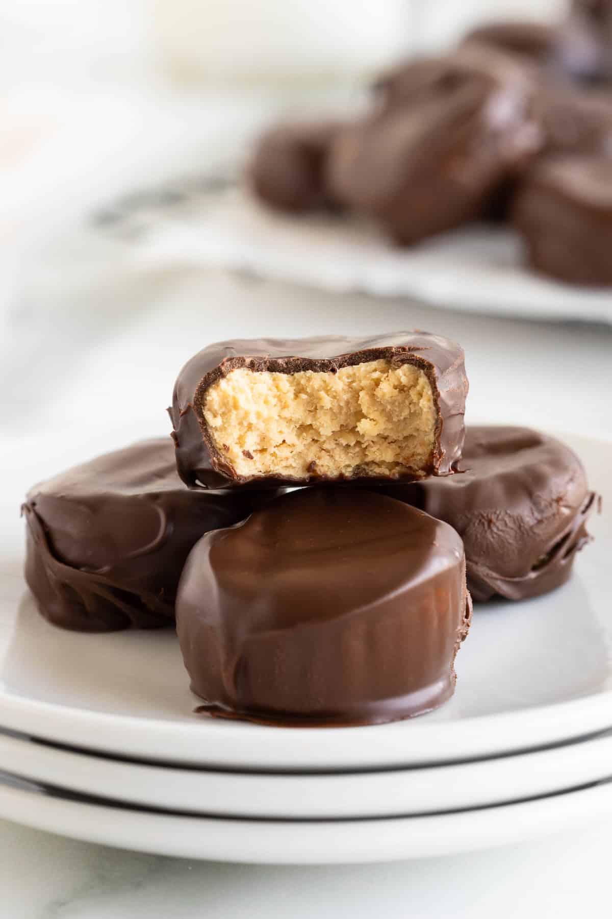 Four peanut butter cups on a stack of three small white plates. The top peanut butter cup has a bite out of it.