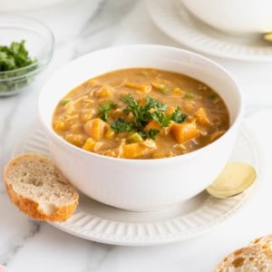 A white bowl of pumpkin pot pie soup on a white fluted plate.