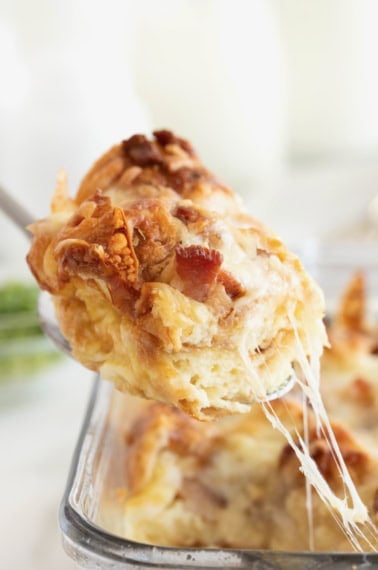 A spoonful of croissant breakfast casserole bing lifted from a glass dish.