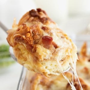 A spoonful of croissant breakfast casserole bing lifted from a glass dish.