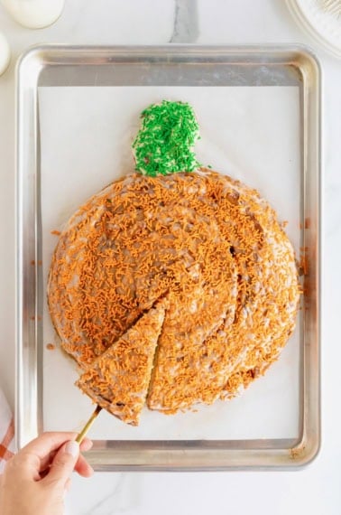 A giant pumpkin-shaped cinnamon roll on a parchment lined aluminum baking sheet.