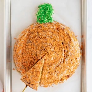 A giant pumpkin-shaped cinnamon roll on a parchment lined aluminum baking sheet.