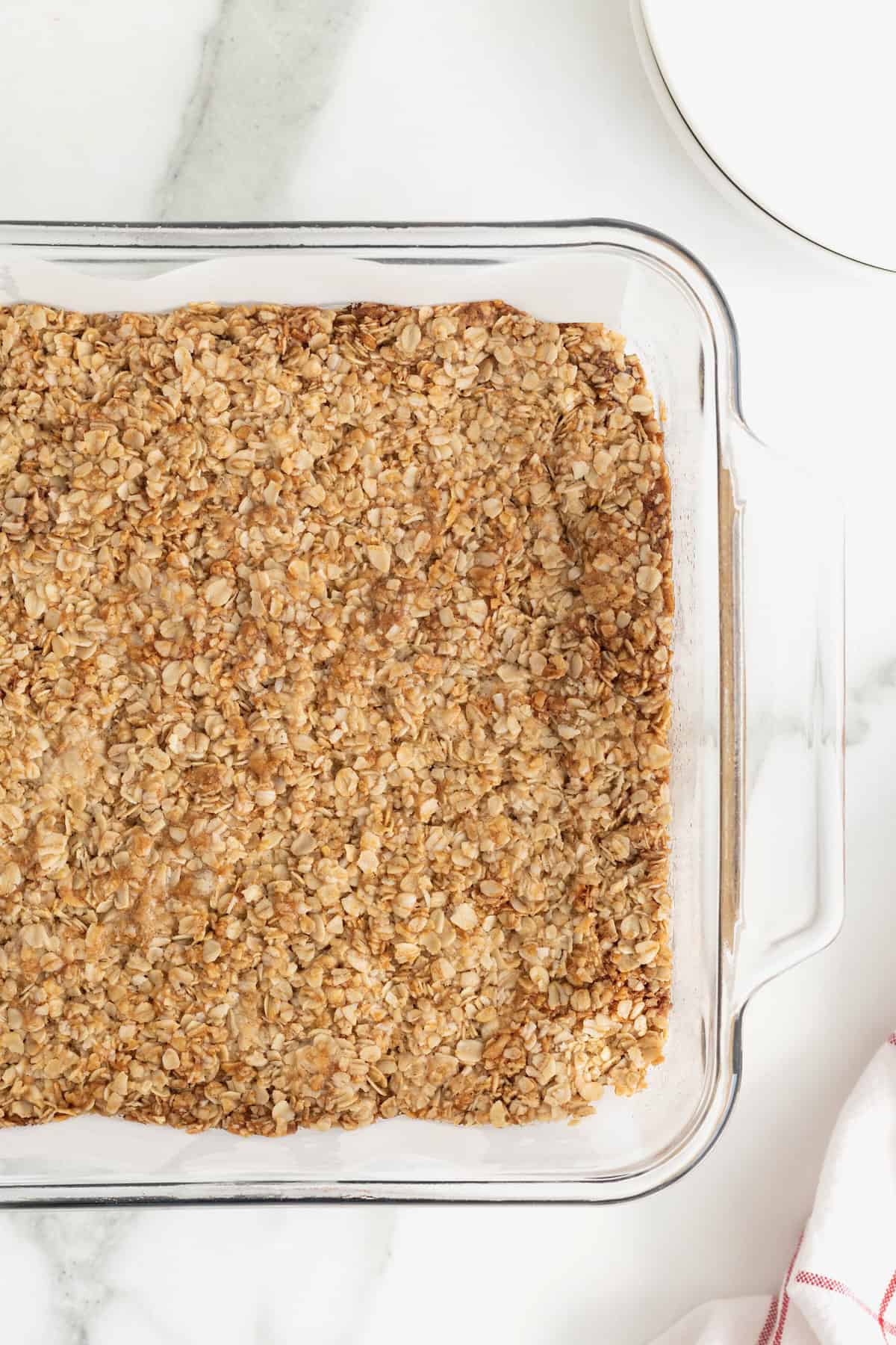 A glass baking dish of oatmeal crunchies on a white marble counter.