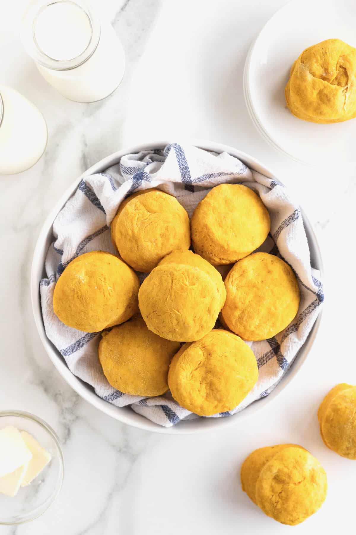 A large white serving bowl lined with a tea towel full of pumpkin biscuits.