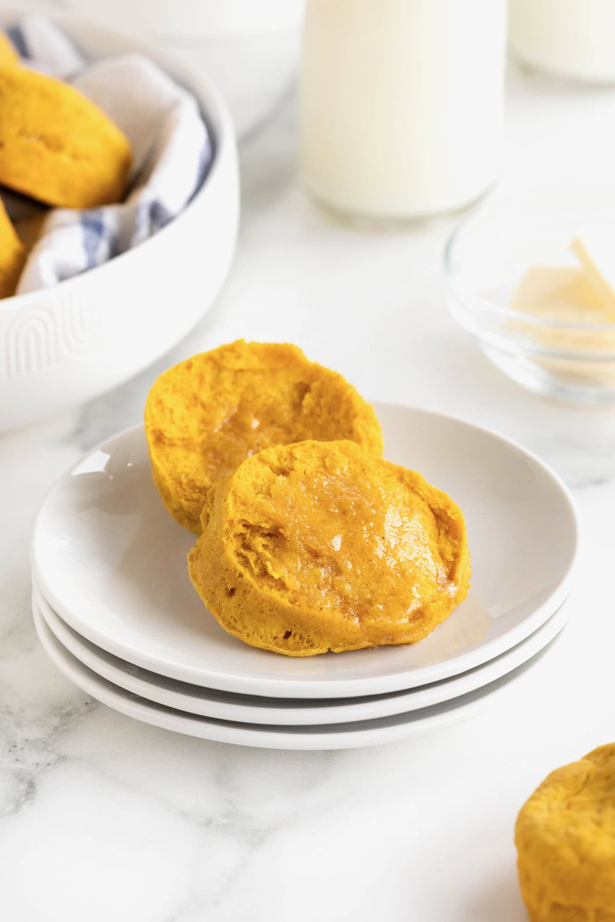 A pumpkin biscuit cut in half on a stack of three small white plates.