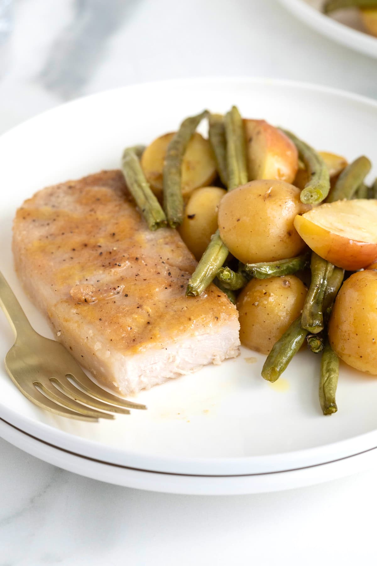 A pork chop on a white dinner plate with gold potatoes and green beans.