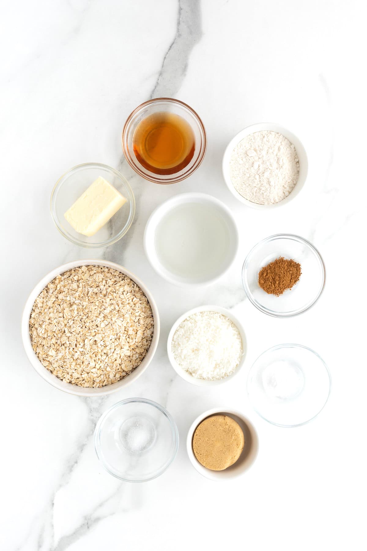 Ingredients to make oatmeal crunchies in small glass dishes on a white marble counter.