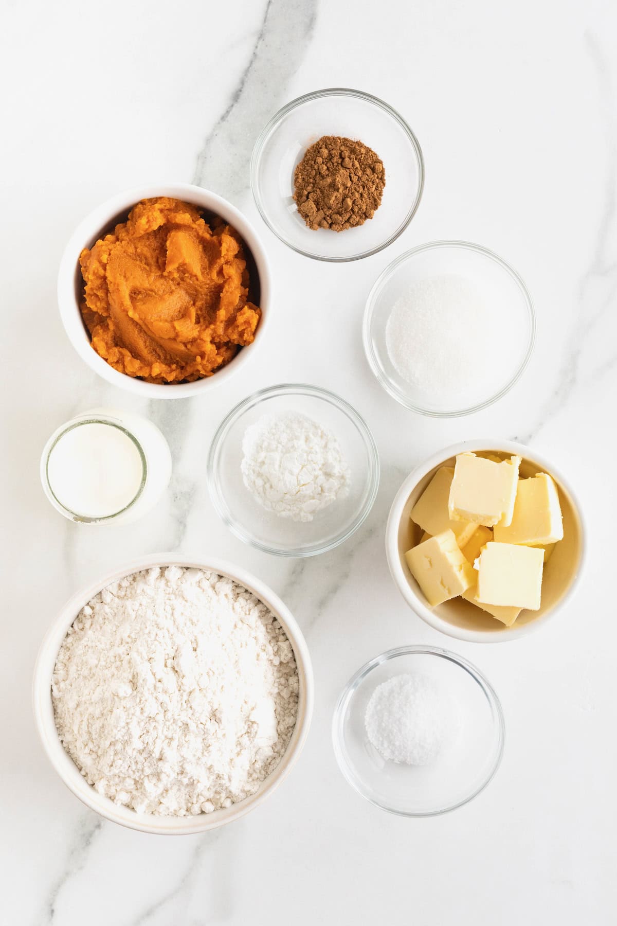 Ingredients to make pumpkin biscuits in small glass dishes on a white marble counter.