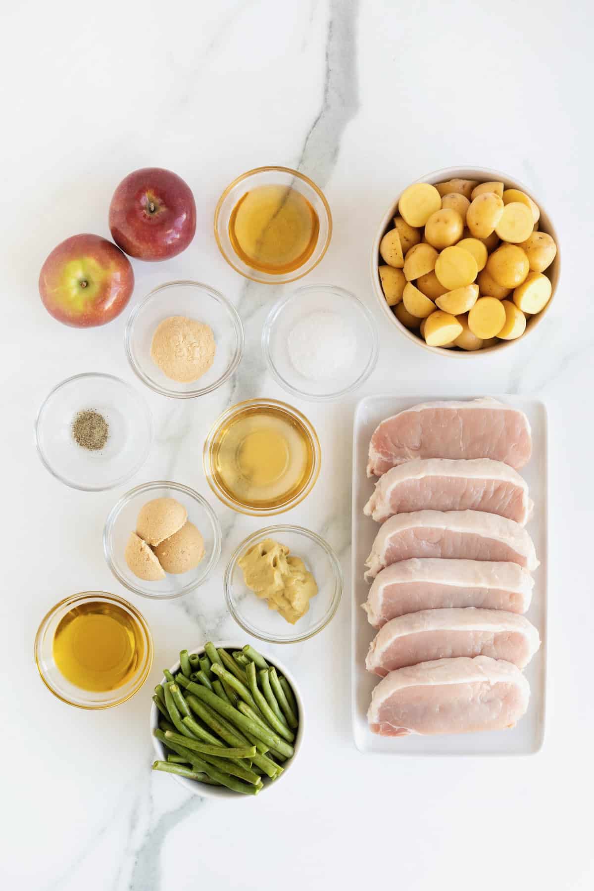 Ingredients to make sheet pan pork chops in small glass dishes on a white marble counter.