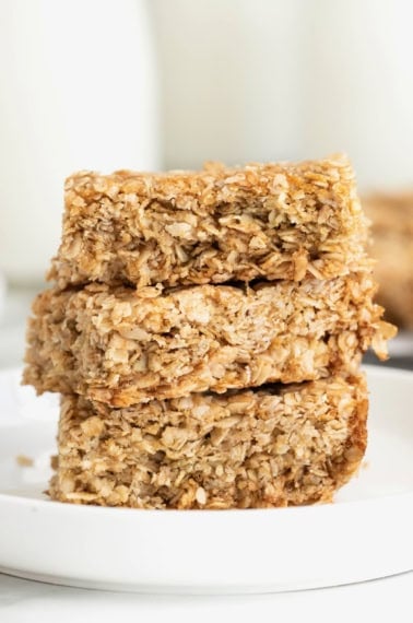 Three crunchy oatmeal bars stacked on a small white plate.