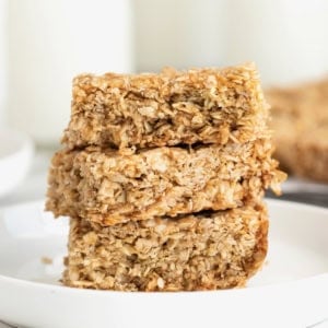 Three crunchy oatmeal bars stacked on a small white plate.