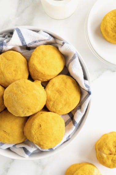 A large white serving bowl lined with a tea towel filled with pumpkin biscuits.