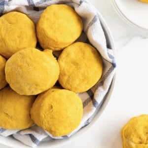 A large white serving bowl lined with a tea towel filled with pumpkin biscuits.