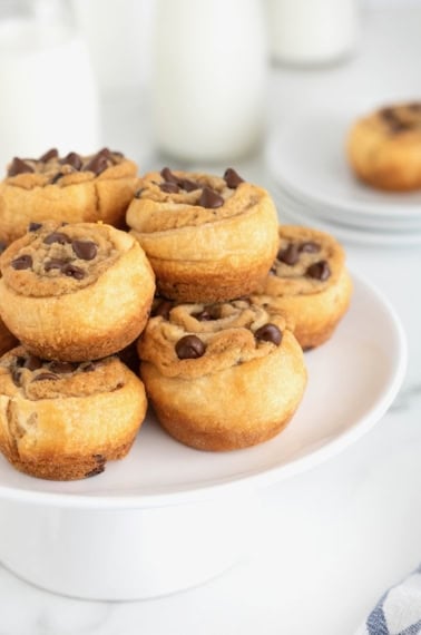 A large white plate stacked with chocolate chip cookie dough cruffins.