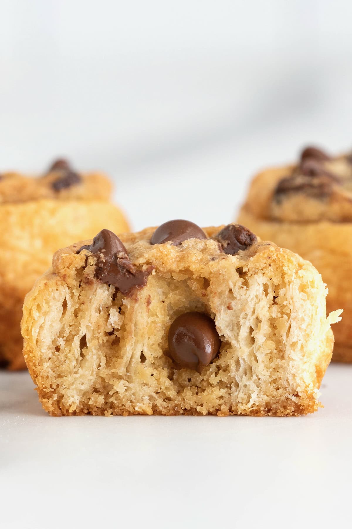 A chocolate chip cookie dough cruffin on a parchment lined cooling rack. The cruffin is cut in half to reveal the inside layers.