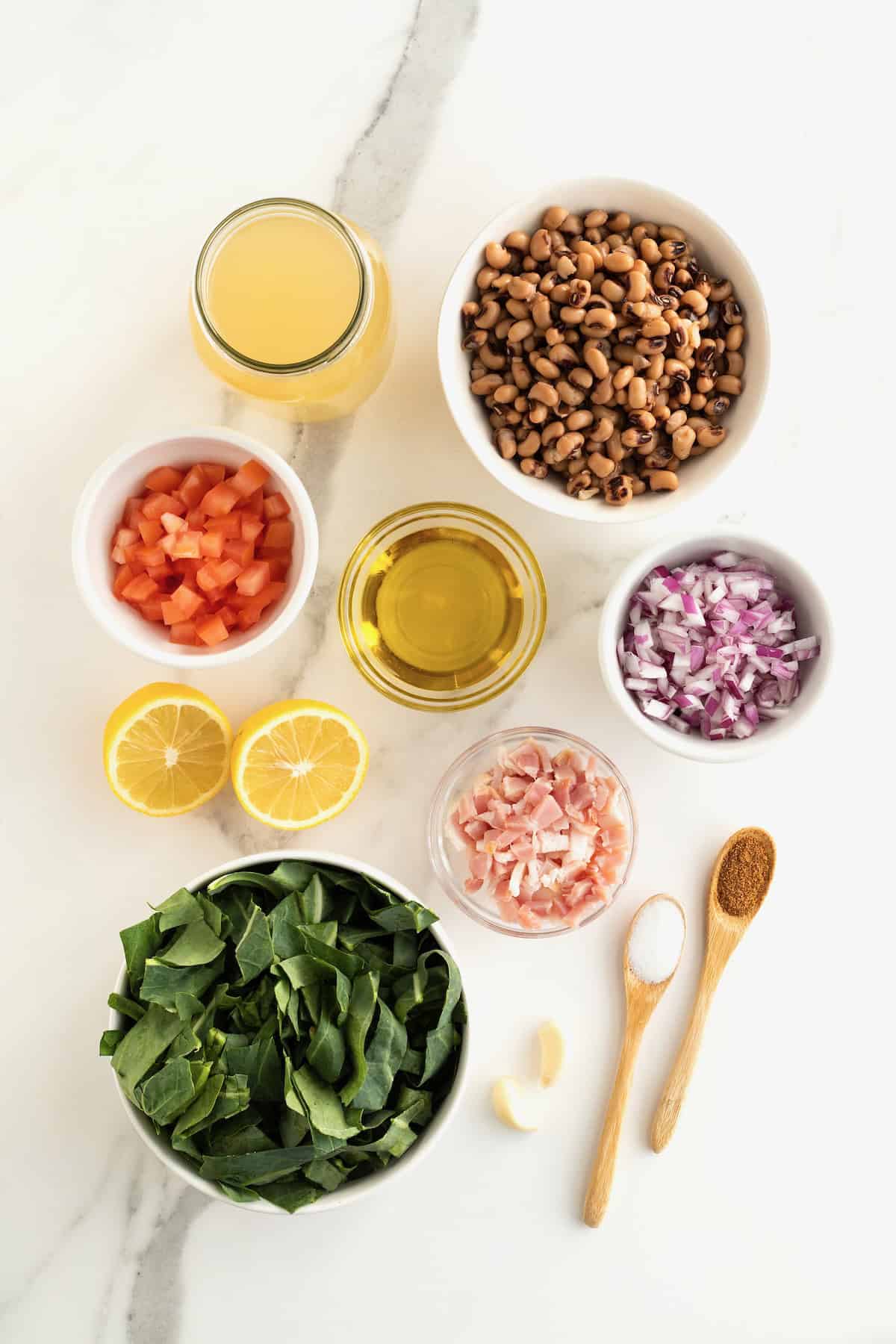 Ingredients to make black eyed peas and collared greens in small glass dishes on a white marble counter.