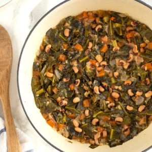 A large white dutch oven filled with black eyed peas and collard greens.