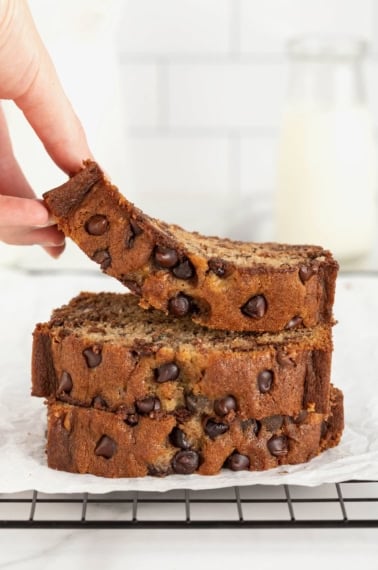 Three slices of chocolate chip banana bread in a stack. A hand is lifting off the top slice.