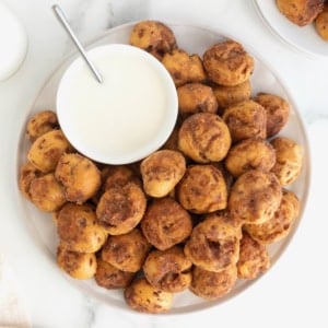 A large white serving plate of cinnamon roll bites with a white bowl of icing.