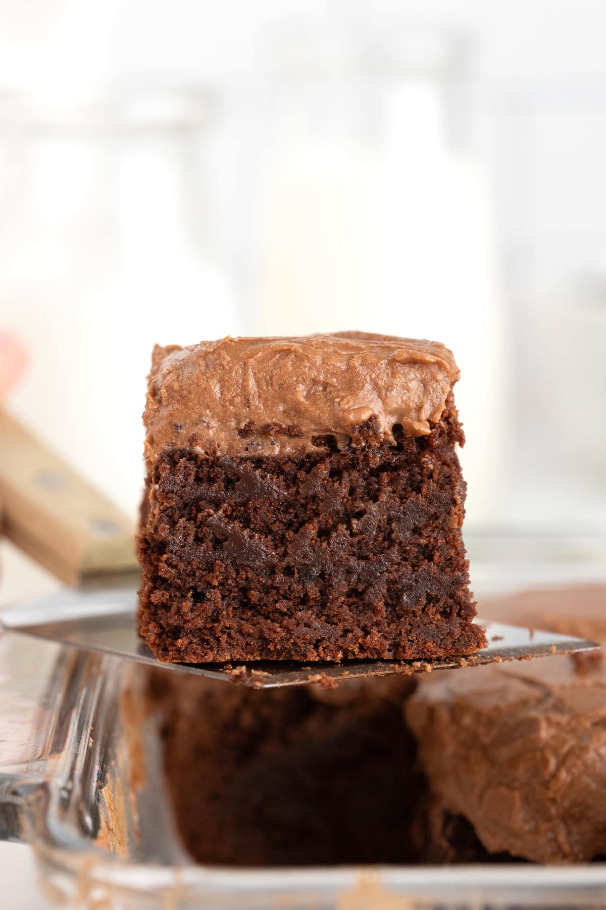 An espresso brownie with frosting being lifted from a baking dish on a wooden handled spatula.