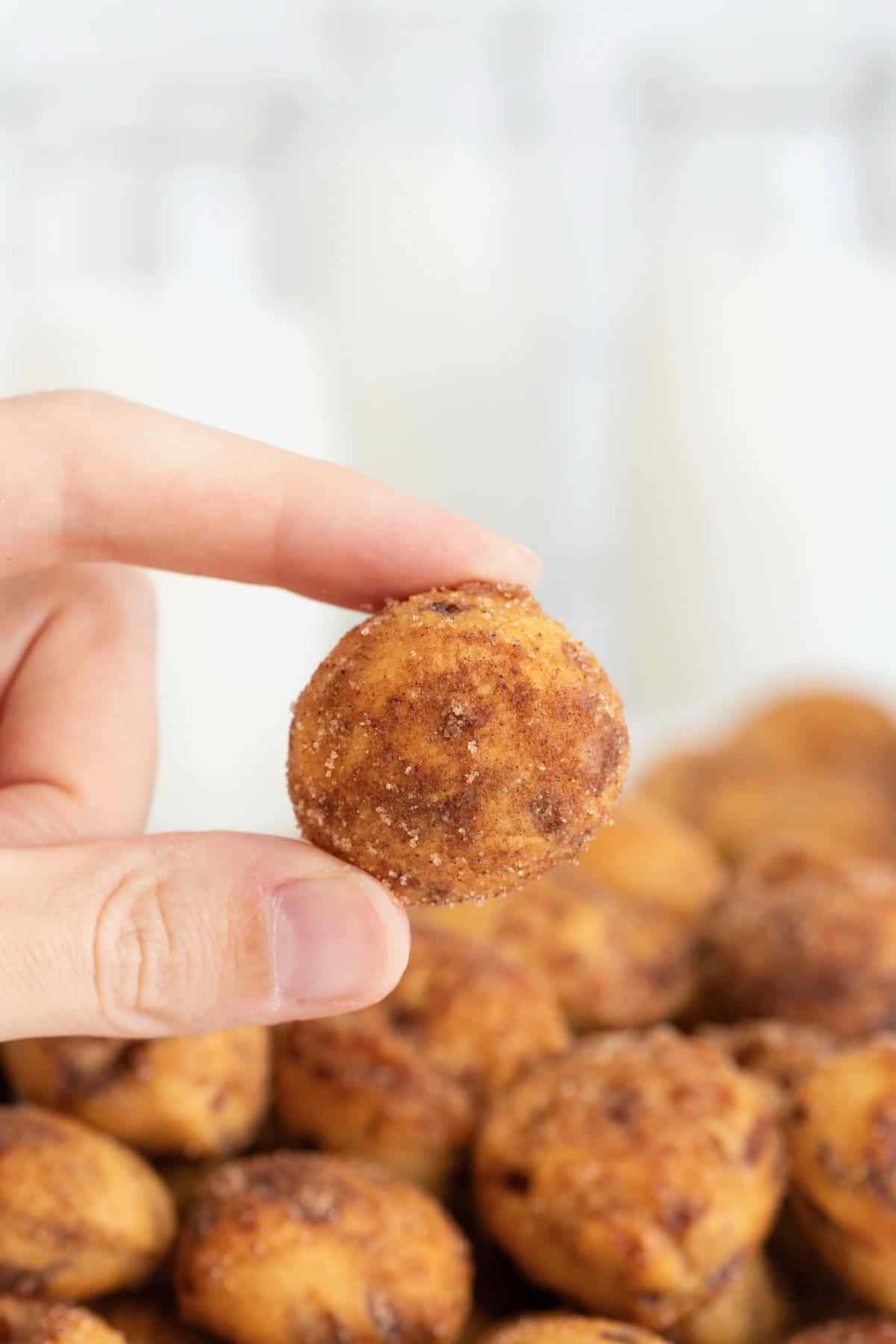 A hand holding a cinnamon roll bite between thumb and forefinger.