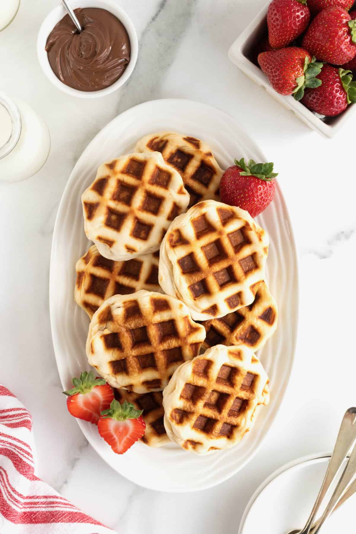 An oblong serving dish filled with round waffles on a white marble counter.