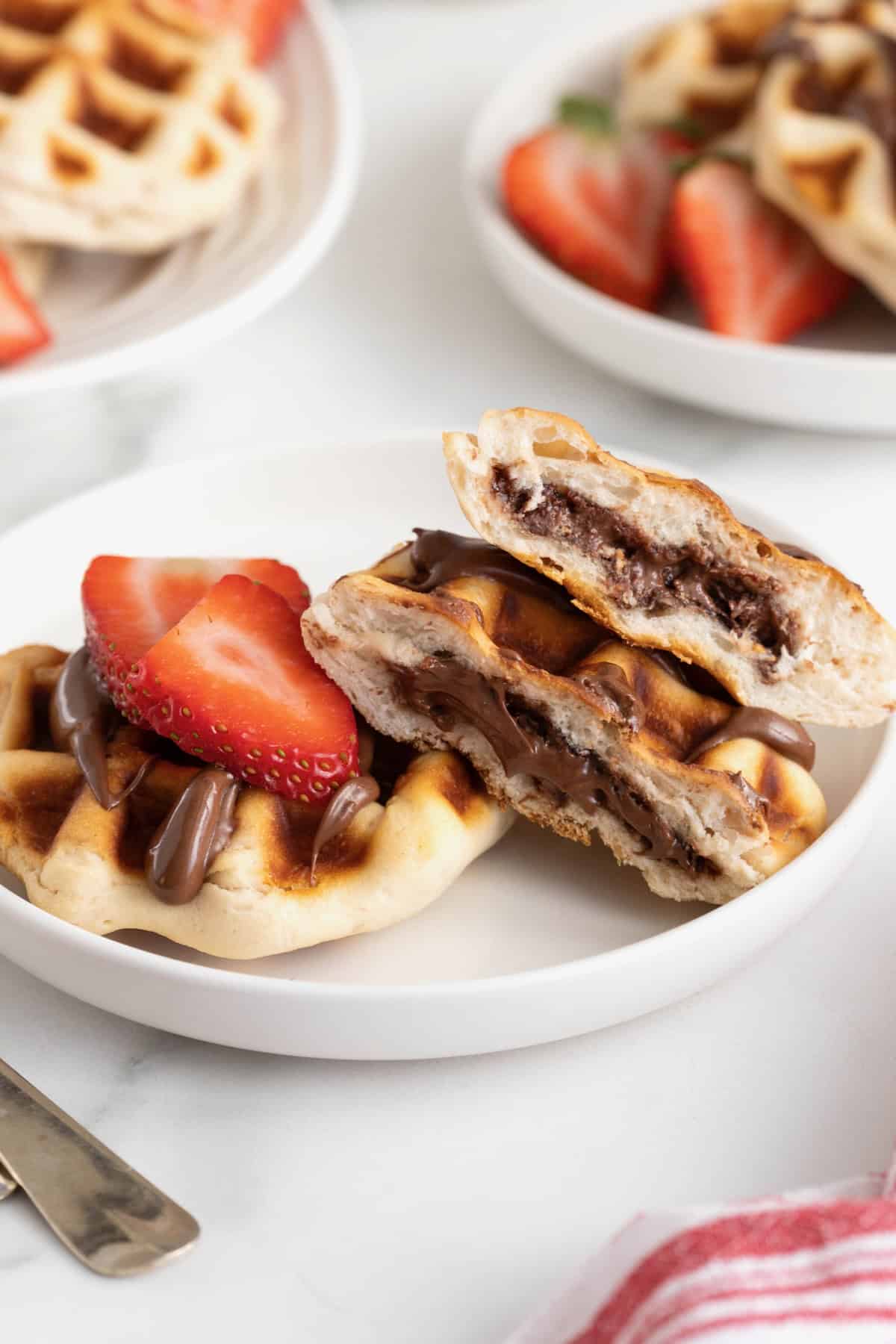 Two Nutella waffles on a white rimmed plate with sliced strawberries on top.