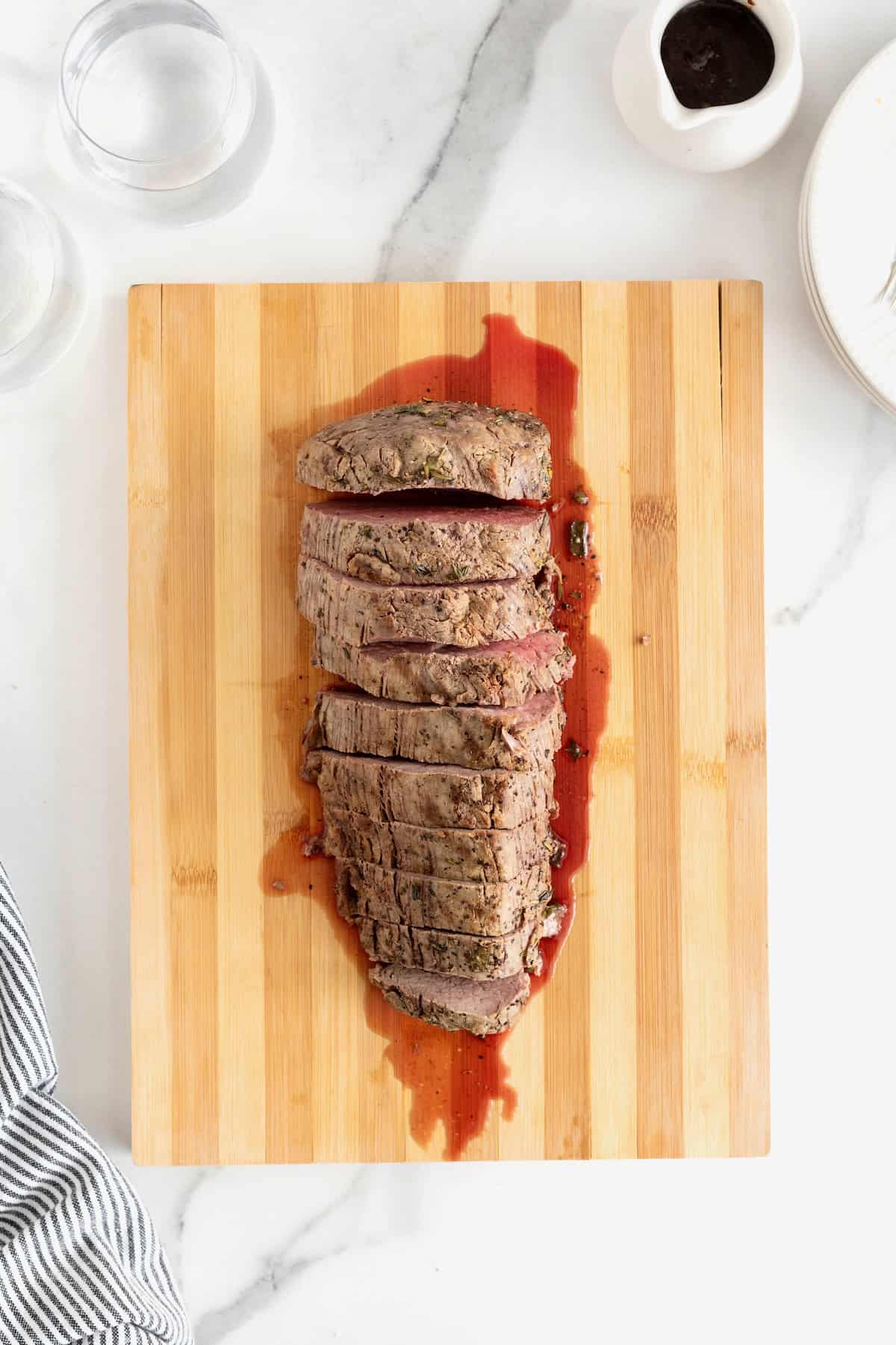 Roasted beef tenderloin cut into 1-inch thick pieces on a wood cutting board.