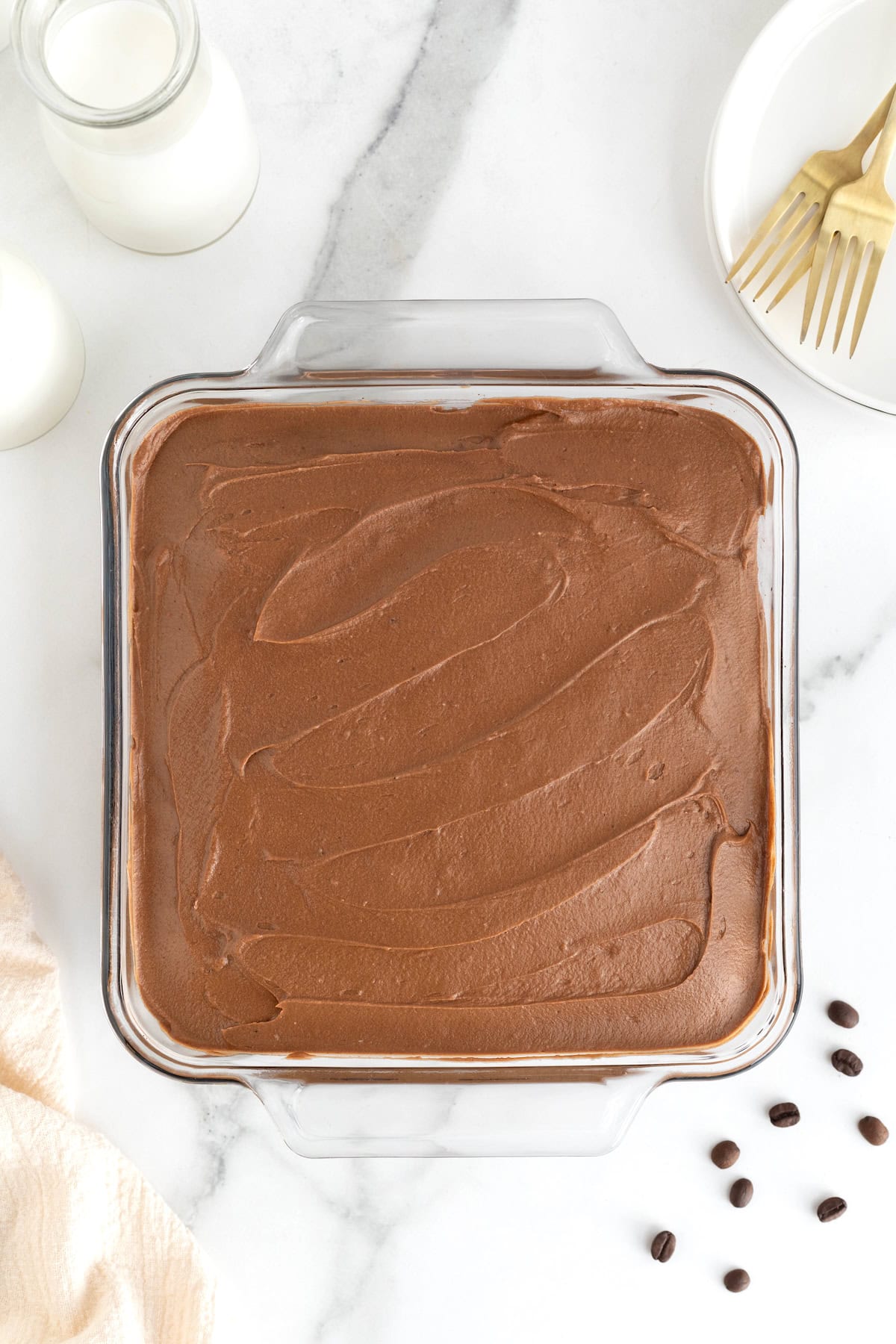 A square glass baking dish of frosted brownies on a white marble counter. 