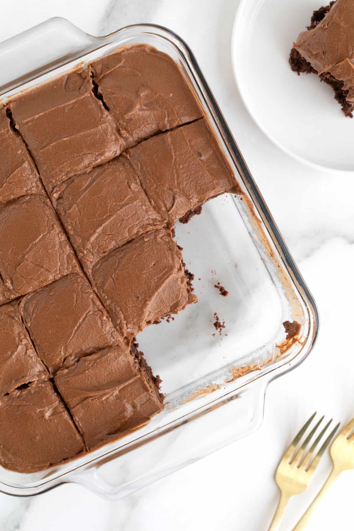 A square glass baking dish of frosted brownies. The three corner brownies are missing.