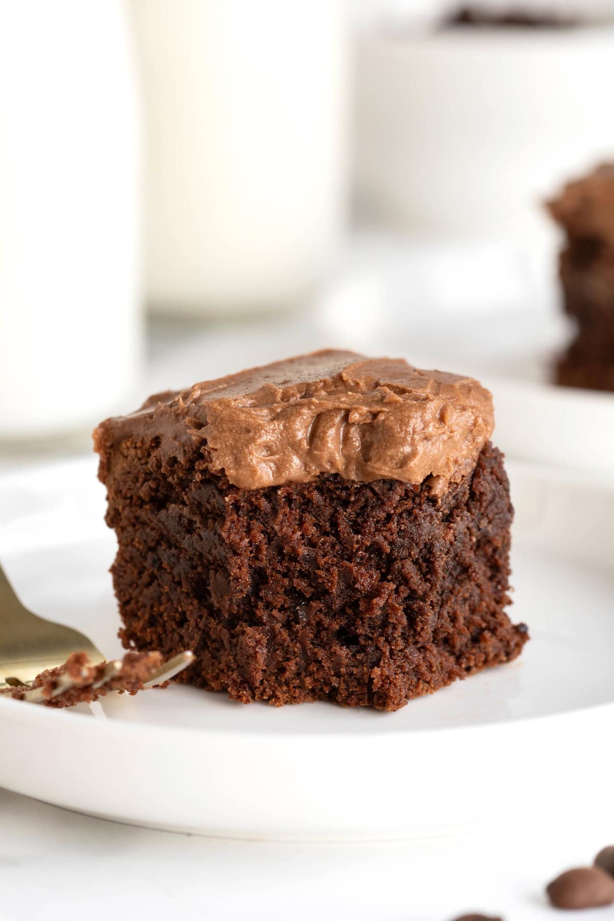 A frosted brownie on a small white rimmed plate next to a fork.