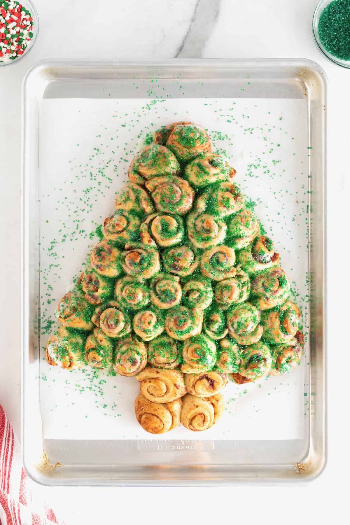 A cinnamon roll Christmas tree sprinkled with green sugar crystals on a parchment lined baking sheet.