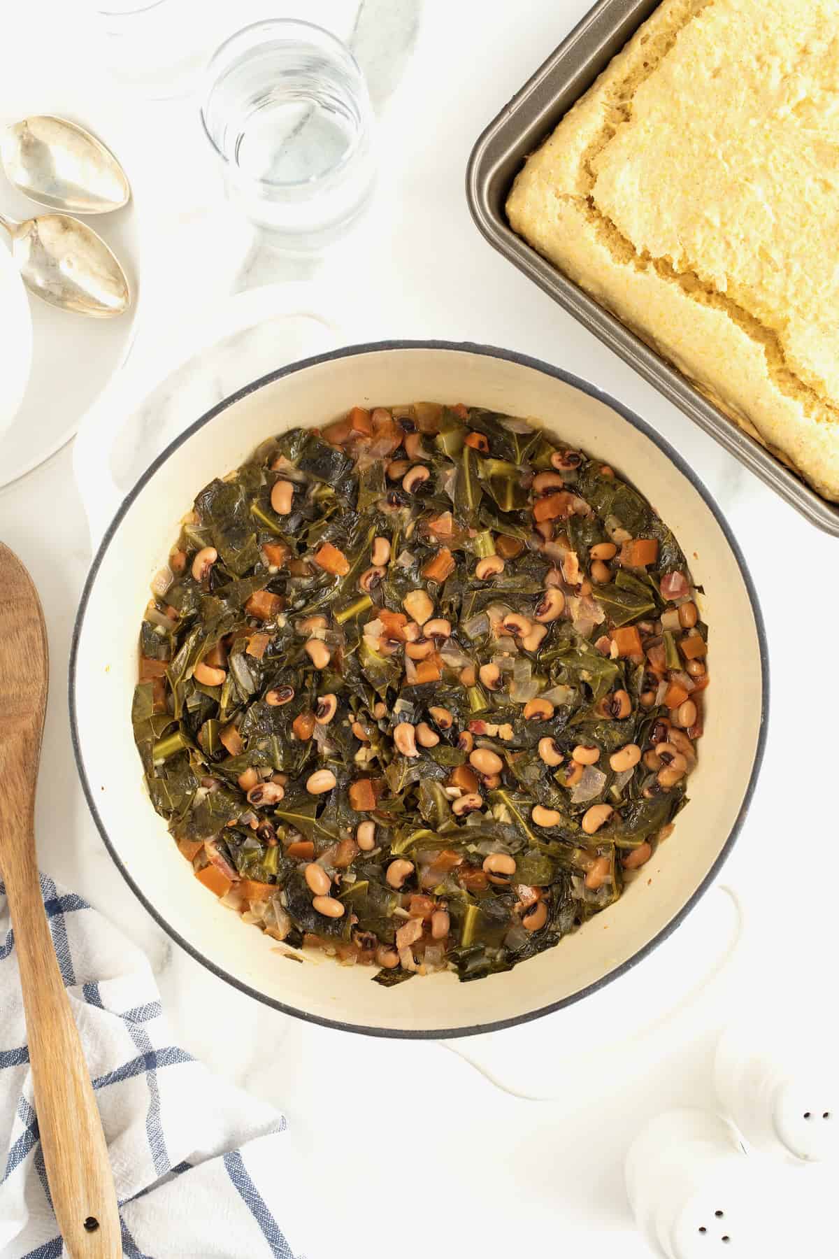 A pot of black eyed peas next to a pan of cornbread on a white marble counter.