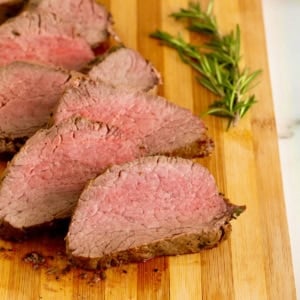 Sliced beef tenderloin on a wood cutting board.