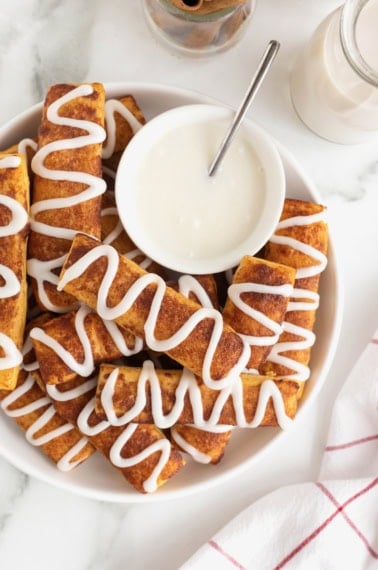 A large white serving polate of cinnamon roll sticks surrounding a bowl of white icing.