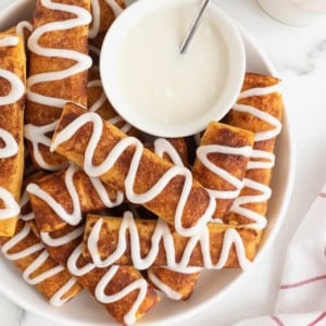 A large white serving polate of cinnamon roll sticks surrounding a bowl of white icing.