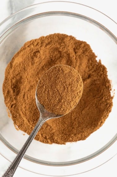 A spoonful of pumpkin pie spice over a glass bowl of mixed spices.