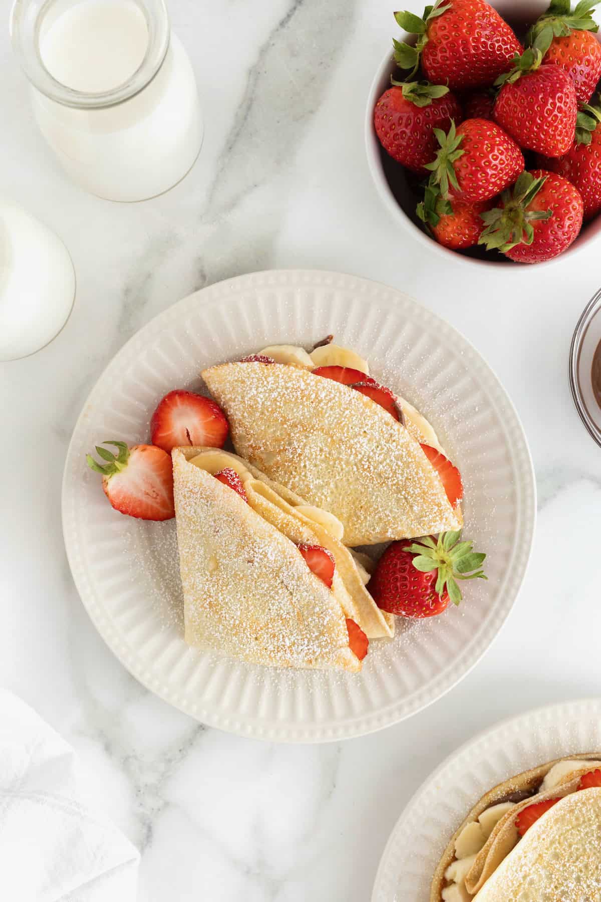 Two crepes dusted with powdered sugar on a white plate.