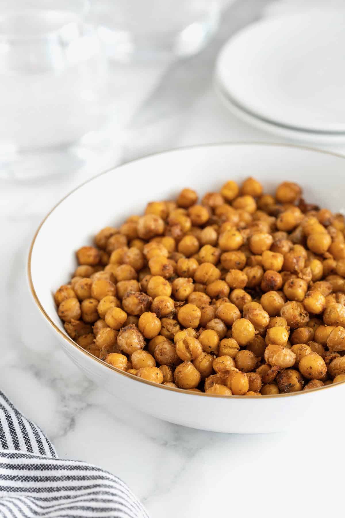 A large white serving bowl of roasted chickpeas on a white marble counter.