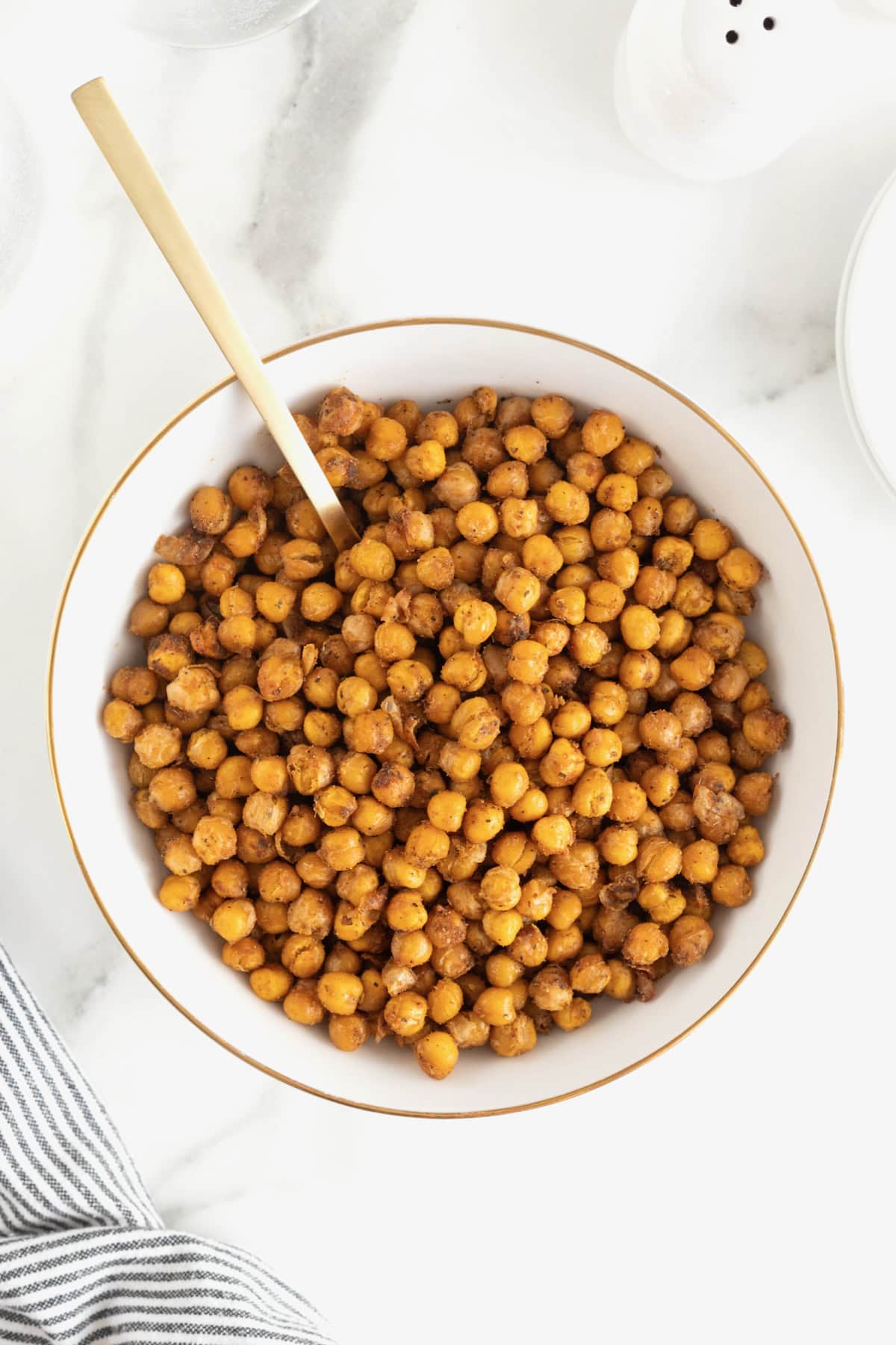 A large white serving bowl of roasted chickpeas on a white marble counter.