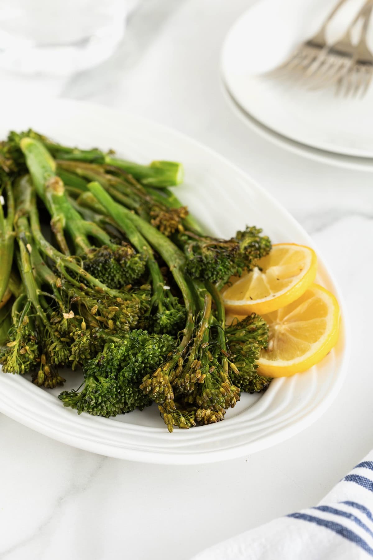 A white oval serving platter of broccolini and lemon slices.