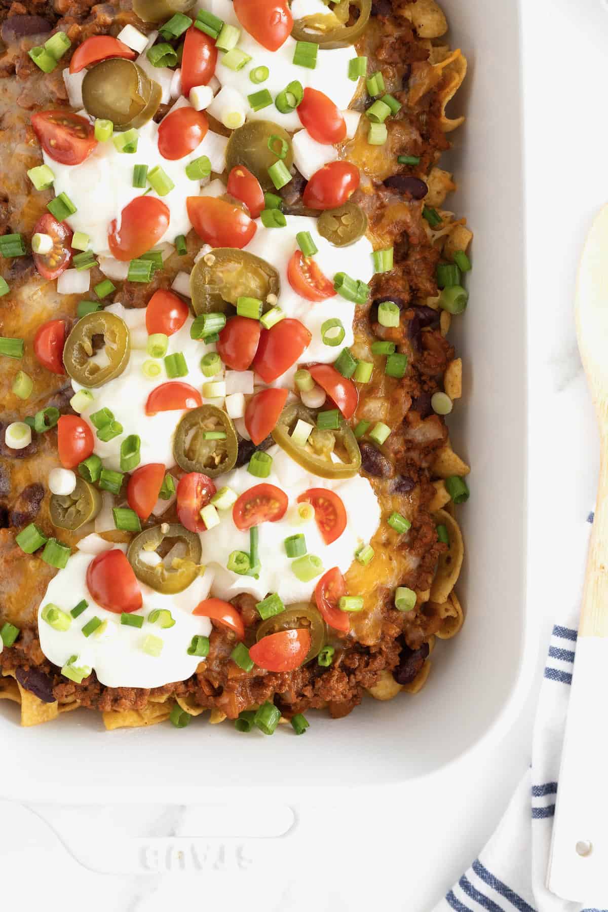 A white casserole dish of Frito Chili Pie casserole o a white marble counter.