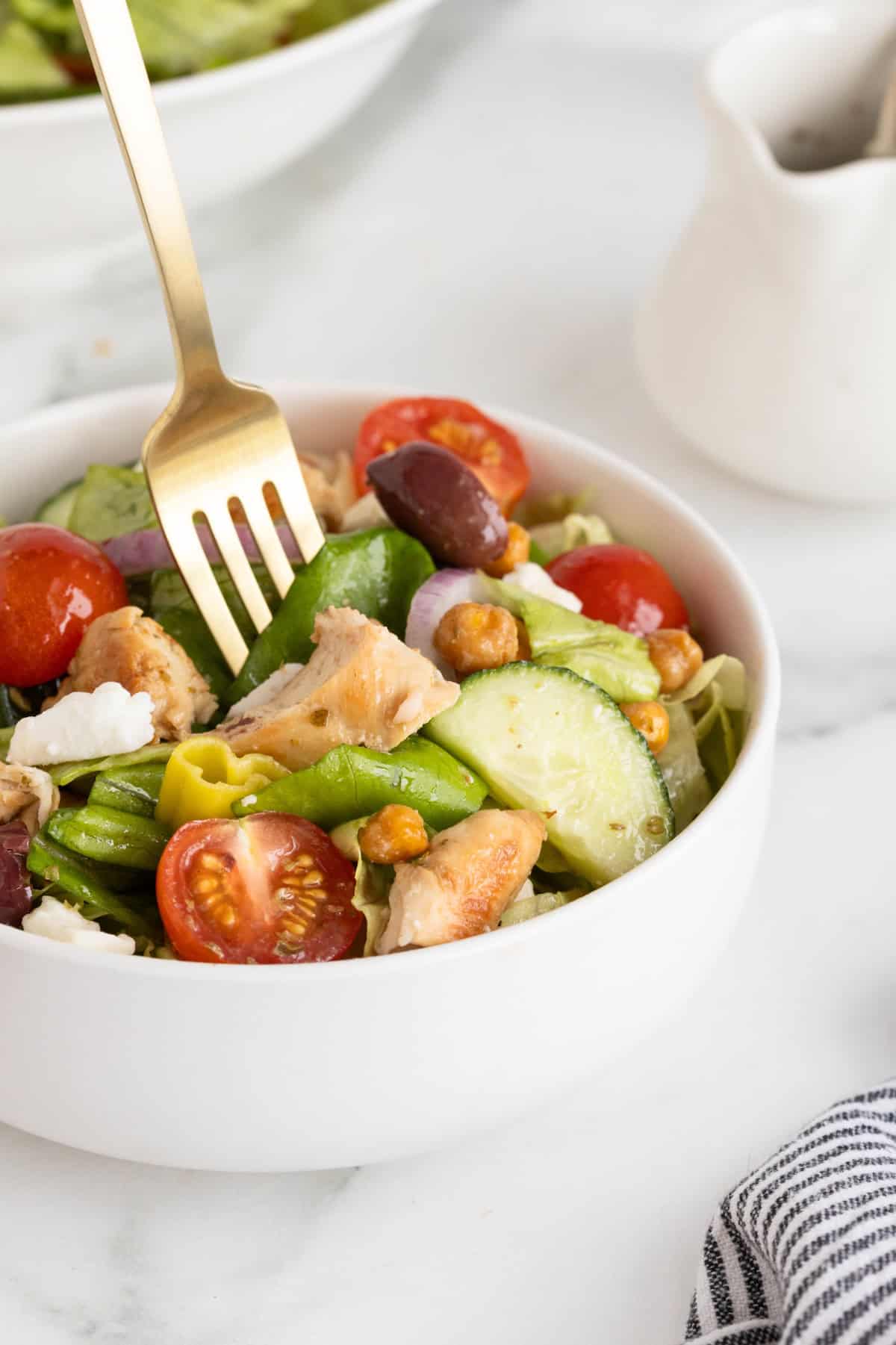 A white bowl of salad with cherry tomatoes, Greek olives, feta, roasted chickpeas and chicken.