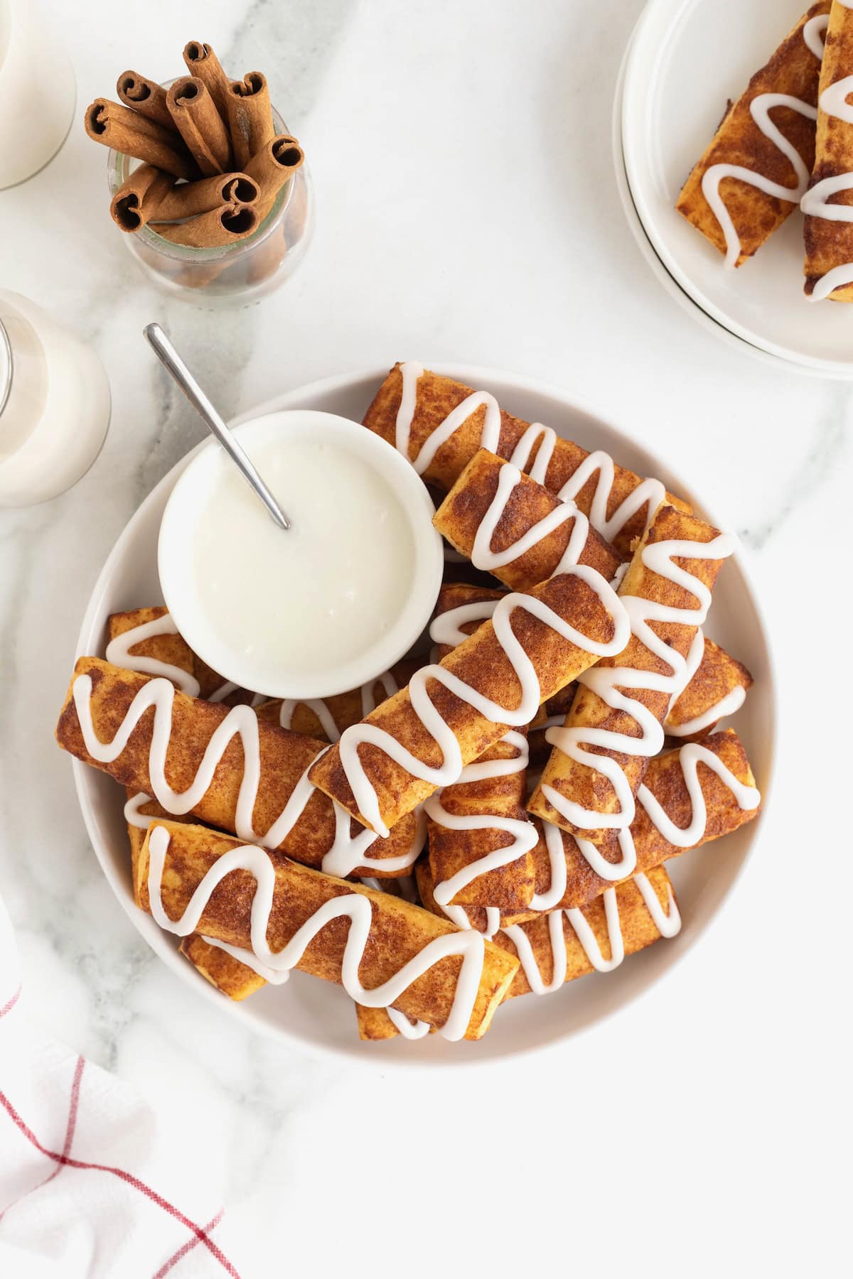 A large white serving polate of cinnamon roll sticks surrounding a bowl of white icing.