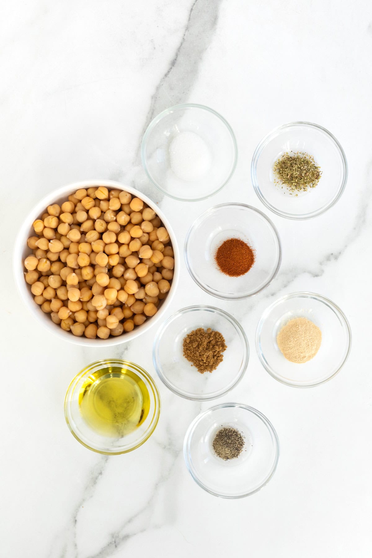 Ingredients to make roasted chickpeas in small glass dishes on a white marble counter.