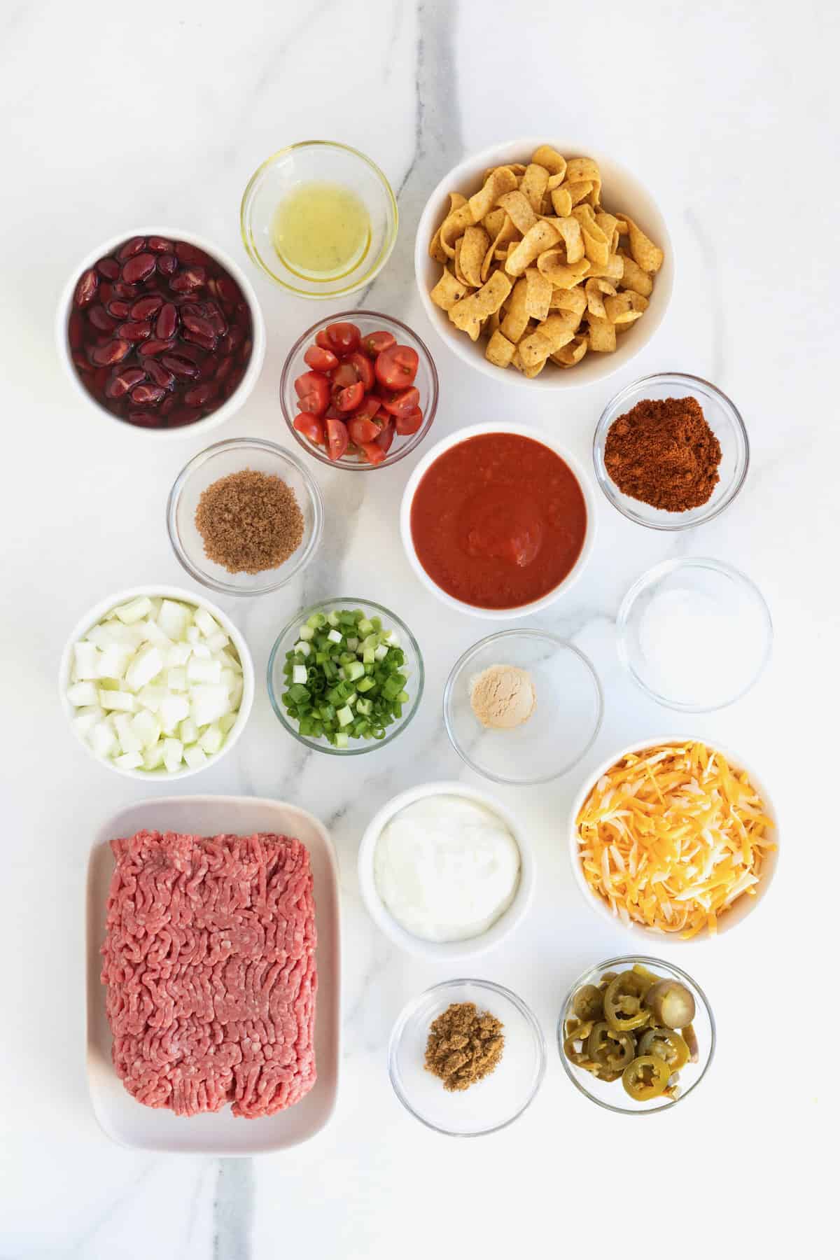 Ingredients to make Frito Chili Pie Casserole in small glass dishes on a white marble counter.